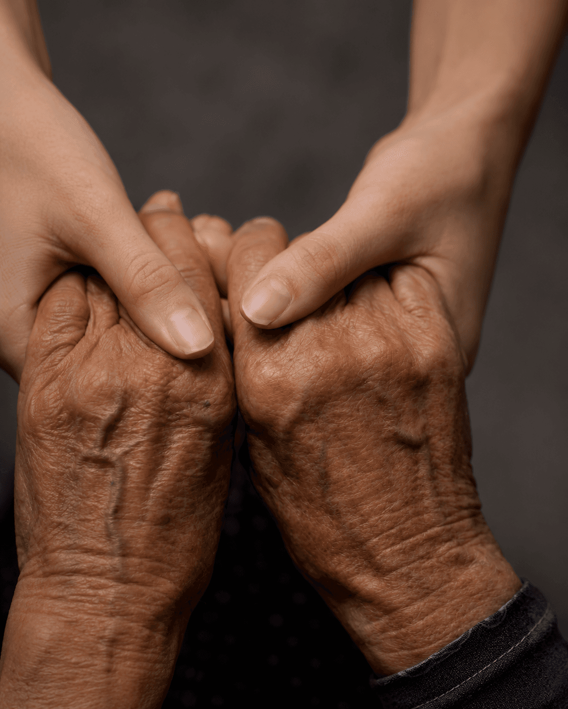 A younger person's hands warmly holding the hands of an older person