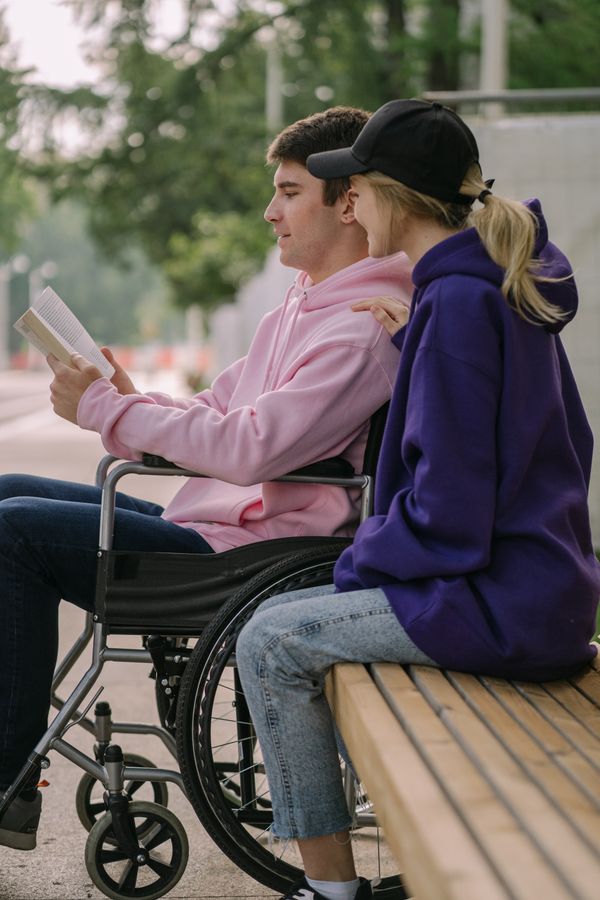A young man using a wheelchair reading with a friend outdoors